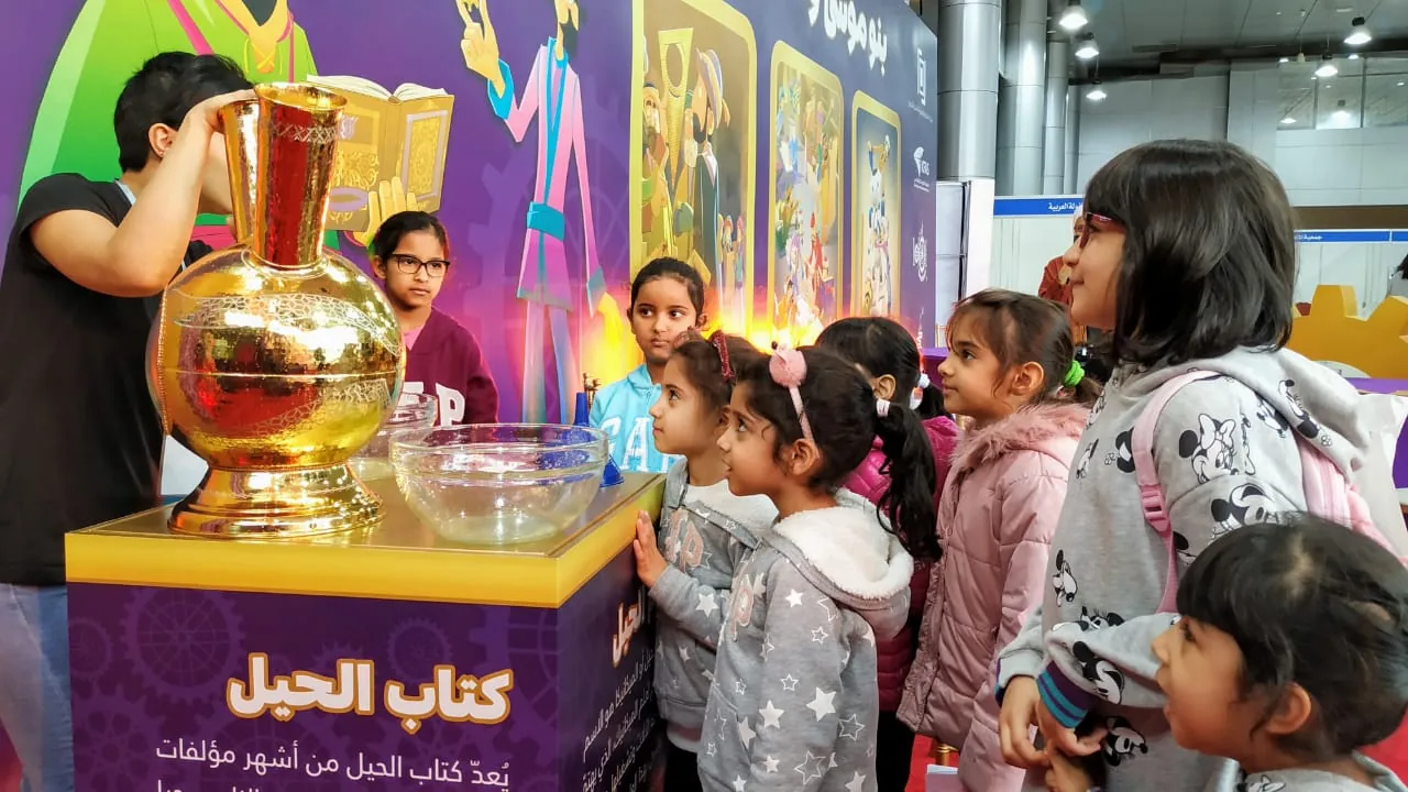 Children watching a demonstration beside a large golden vessel.